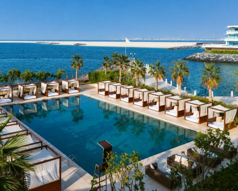 Bvlgari Resort Dubai luxury beach club with waterfront infinity pool, private cabanas, palm trees, and Arabian Gulf views on Jumeirah Bay Island.